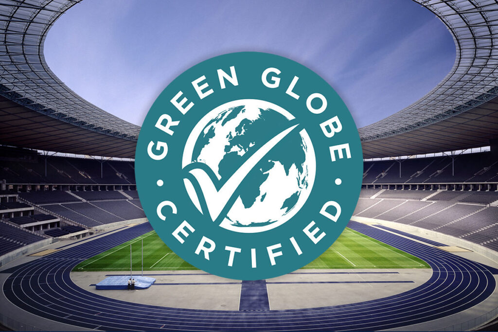 Das türkis-weiße Logo „GREEN GLOBE CERTIFIED“ ist zentral über eine Innenansicht des Olympiastadions Berlin mit seiner blauen Laufbahn und dem Rasenplatz gelegt.